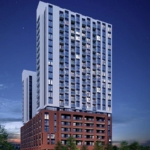 1989 Condominium A tall, modern apartment building from 1989 with a combination of red brick and white concrete facade, illuminated at night. Multiple windows and balconies are visible. The surrounding area has small trees and parked cars, with a twilight sky in the background.