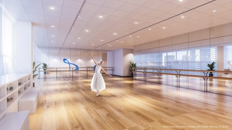 A dancer in a white ballet dress practices gracefully in a spacious, well-lit studio with wooden floors and mirrored walls. Large windows overlook a cityscape dotted with new condos. Potted plants and a blue ribbon decoration add charm to this urban oasis.