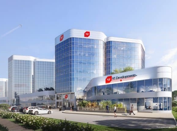 A modern office building with a reflective glass facade, labeled "NF Developments," stands amidst lush greenery and a bustling parking lot. It mirrors the ambitions of Gagan Bector in pre-construction projects. Above, a clear blue sky and distant airplane trail complete the scene.
