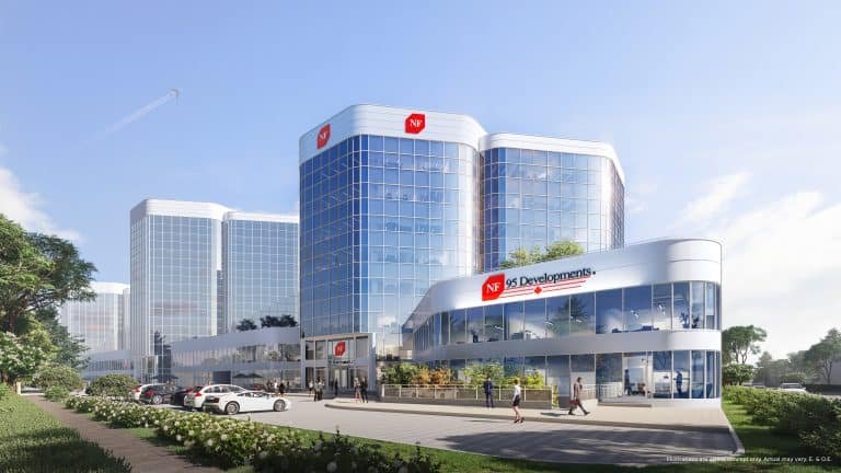 A modern office building with a reflective glass facade, labeled "NF Developments," stands amidst lush greenery and a bustling parking lot. It mirrors the ambitions of Gagan Bector in pre-construction projects. Above, a clear blue sky and distant airplane trail complete the scene.