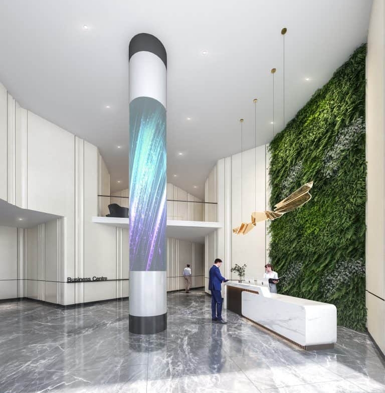 A modern office lobby with a sleek, white reception desk hosts two people interacting. A vertical LED display wraps around a column, while a green wall with plants decorates one side. The lively atmosphere is reminiscent of the innovative design found in new condos across the GTA.