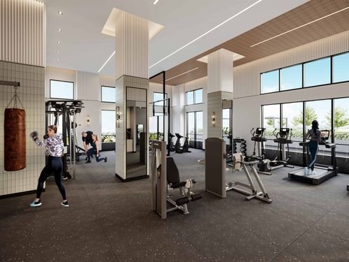 A modern gym in the heart of new condos in GTA boasts large windows, exercise equipment like treadmills, weight machines, and a punching bag. The space is bright, with high ceilings and contemporary decor.