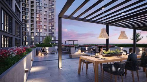 On the rooftop terrace, a wooden dining table and chairs sit under a pergola, illuminated by hanging lamps. People gather in cozy sections, surrounded by city buildings during sunset. This serene escape is perfect for envisioning life in new homes in GTA.