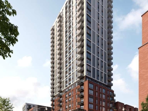 A modern high-rise building with a mix of red brick and glass facade, offering stunning new condos. The structure features numerous balconies and large windows. Street-level view shows people walking and trees lining the sidewalk under a clear blue sky.