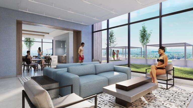 Modern lounge in new condos with blue sofas and a patterned rug. People relax and socialize inside and on the sunlit terrace, which features pergolas and a skyline view. Large floor-to-ceiling windows provide natural light and outdoor scenery, enhancing the allure of new homes in the GTA.
