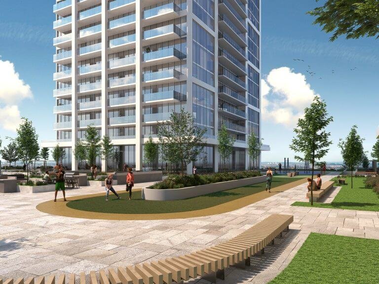 A modern high-rise, featuring sleek glass windows, stands beside a landscaped recreational area with a pathway, benches, and greenery—ideal for those scouting new condos. People leisurely enjoy the sunny open space while the sky remains clear with a few gentle clouds.