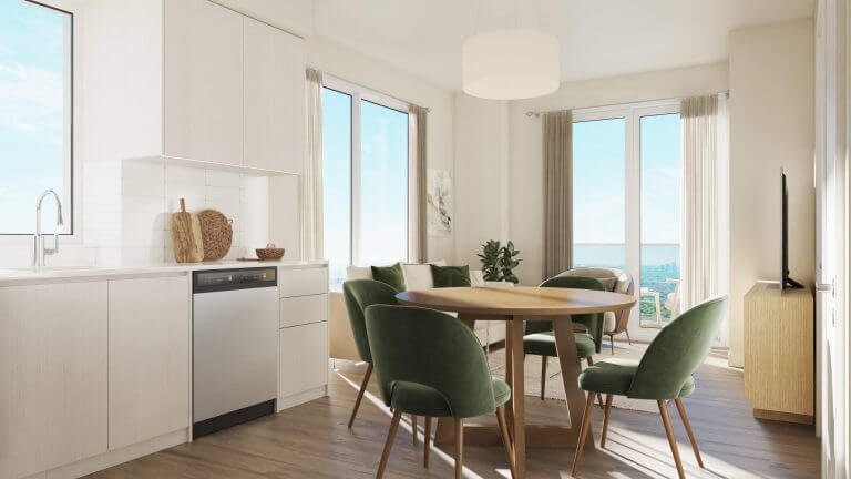 This bright, modern dining area could be yours in one of the new condos by Gagan Bector. Picture a round wooden table with green velvet chairs basking in sunlight streaming through large windows and a glass door, illuminating white cabinetry and wooden floors while a potted plant sits elegantly in the corner.
