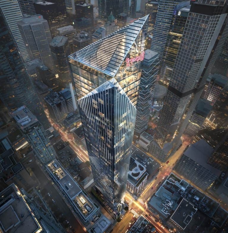 Aerial view of a modern cityscape featuring a tall, geometric skyscraper with a distinct angular design. The building is illuminated against the backdrop of neighboring high-rises and city streets lined with vehicles. Near the top, the sign reading "Freed Hotel" is visible among sleek residences.