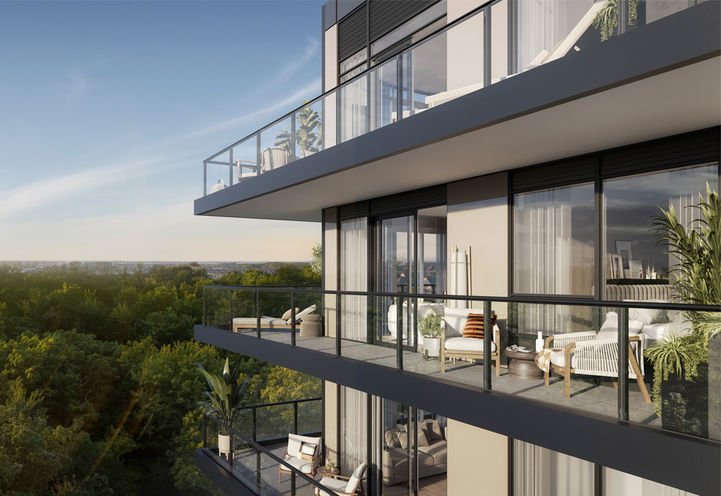 A modern condo building with multiple glass-walled balconies, each furnished with outdoor seating and plants. The structure overlooks a lush green forest under a clear sky. The sun is setting or rising, casting a warm glow over the scene, reminiscent of the serene views along the High Line.