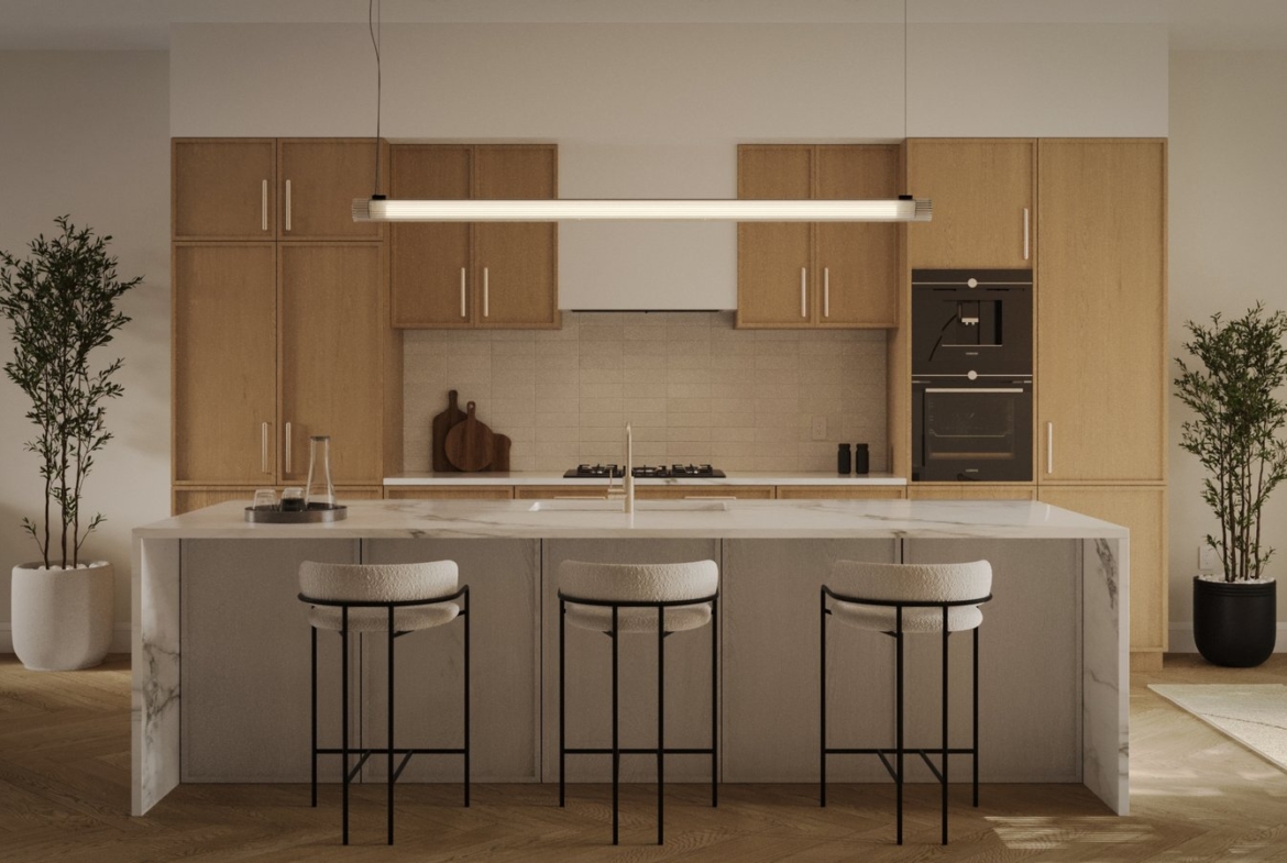 The modern kitchen in new homes in GTA features light wood cabinets, a marble island with three cushioned bar stools, a sleek hanging light fixture, two potted plants, and built-in stainless steel appliances. The room is warmly lit and elegantly organized.