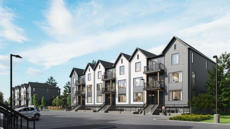 A row of modern, three-story townhouses designed by Gagan Bector stands with gabled roofs and large windows. The buildings, painted in neutral colors, overlook a mostly empty parking lot with a few cars. Under the clear blue sky, these pre-construction homes exude contemporary charm.