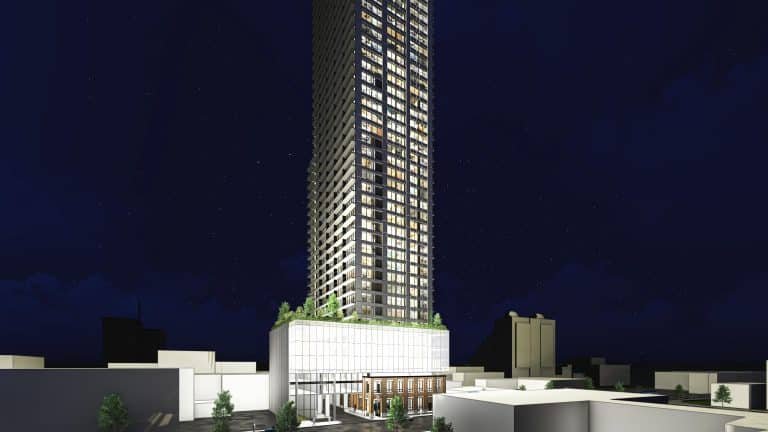 A tall, illuminated skyscraper rises against a dark night sky. The building features a modern design with a glass facade and several floors of glowing windows, resembling the sleek style often seen in new homes in GTA. Surrounding the structure are low-rise buildings and trees.