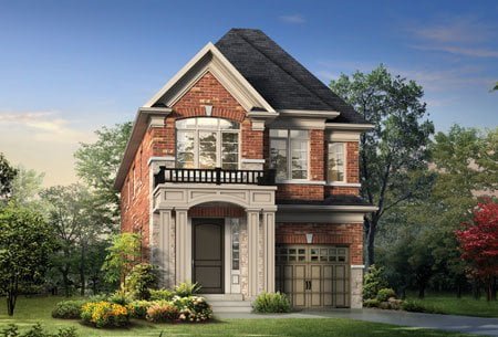 A two-story brick house with a dark gray shingled roof, large front windows, and a small balcony above the entrance. The entrance has a gray door and steps leading up to it. The house is surrounded by a well-manicured lawn, shrubs, colorful flowers, and trails weaving through the trees in the background.