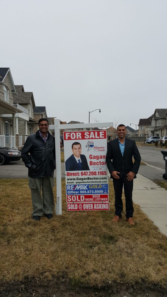 Two men standing in front of a for sale sign.