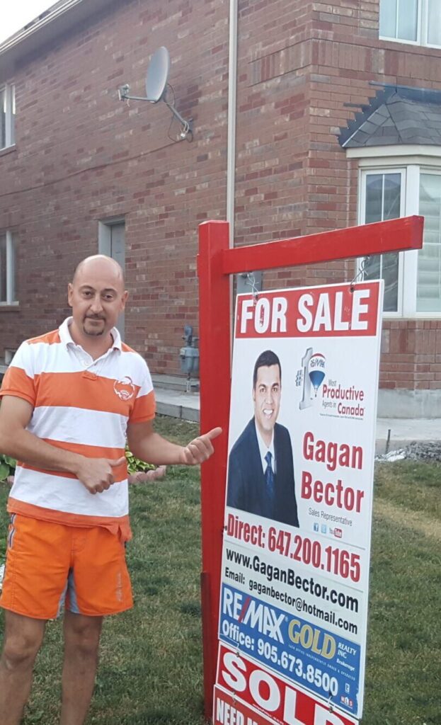 A man standing in front of a house with a for sale sign.
