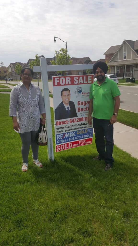 Two people standing in front of a for sale sign.