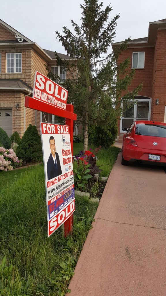 A red car sits in front of a sold sign in front of a house.