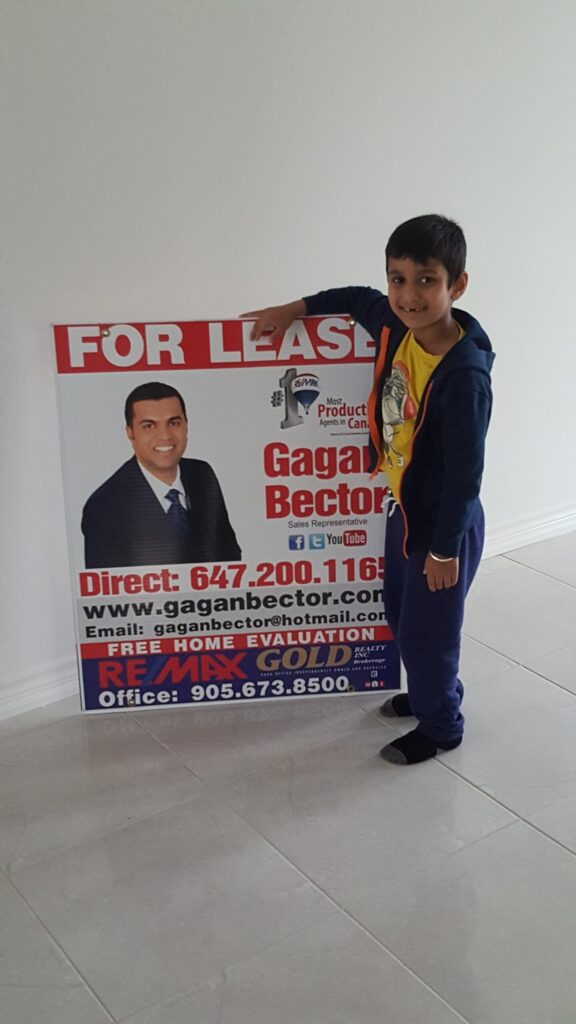 A young boy standing next to a for lease sign.