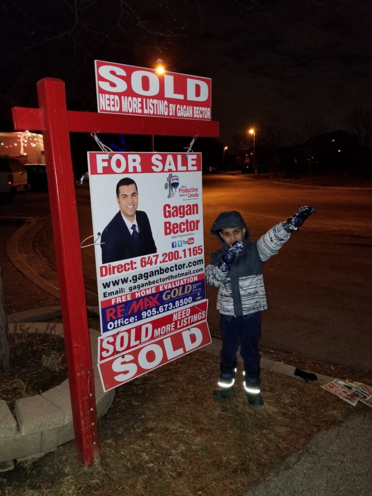 A boy standing in front of a for sale sign.