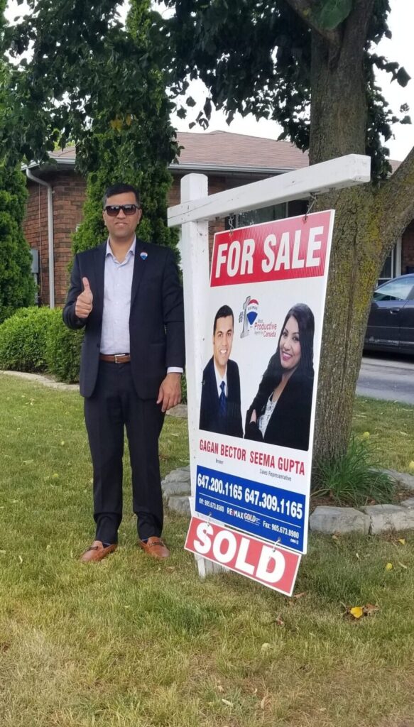 A man standing in front of a house with a real estate sign.