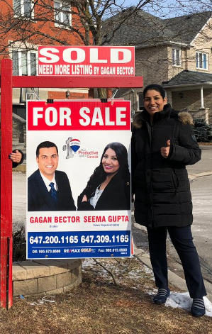 Three people standing in front of a sold for sale sign.