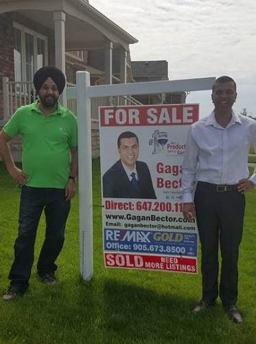 Two men standing in front of a for sale sign.