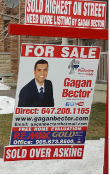 Two men standing next to a for sale sign in front of a house.